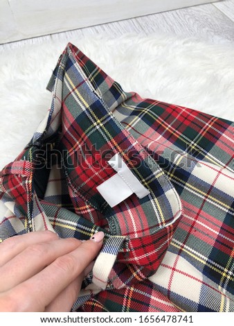 Blank white tag on checkered clothes on a background of white fur close-up