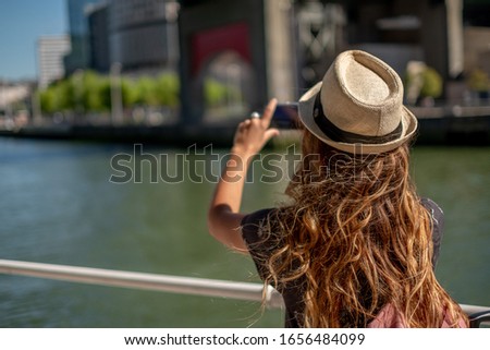 A blonde tourist makes a photo with her mobile phone next to a r
