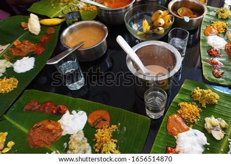 Typical traditional items of a Kerala meal (sadya) on a dining table. Various curries and pickles are arranged on tender banana leaves. Top view.                                