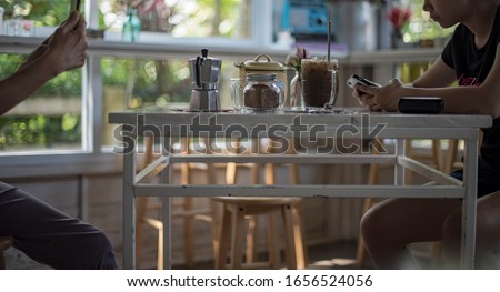 Mom using her mobile phone taking pictures of her daughter watching clips on her mobile phone in a nice and friendly vintage coffee shop. Lovely mom & daughter asian family atmosphere in the morning.