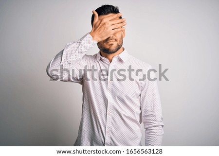 Young handsome man wearing elegant shirt standing over isolated white background covering eyes with hand, looking serious and sad. Sightless, hiding and rejection concept