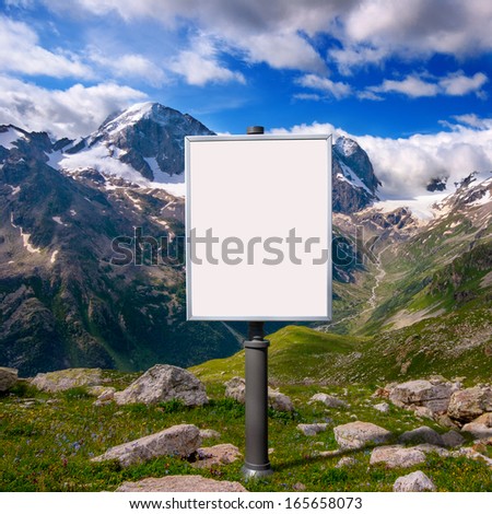 blank billboard for advertising mounted on a meadow among the mountains with snow-capped peaks