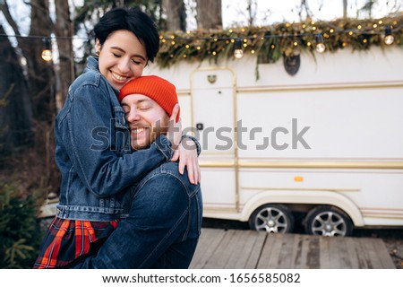 Close up photo of a happy and  hugging couple against the background of their trailer on which they are travel