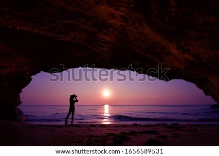 woman standing using camera to take a picture in front of the cave in the morning at sunrise