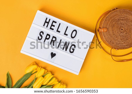 Hello Spring text on a display lightbox with yellow tulips on bright background.