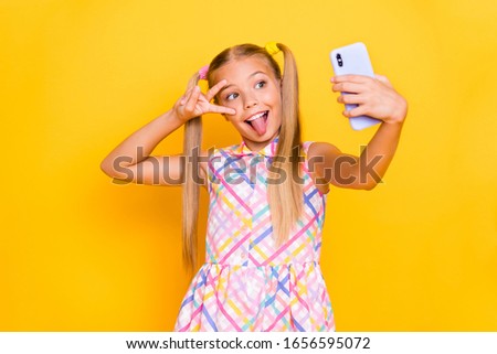 Photo of pretty small lady hold telephone influencer make selfies blog showing v-sign symbol stick tongue out mouth wear checkered summer dress isolated bright color background