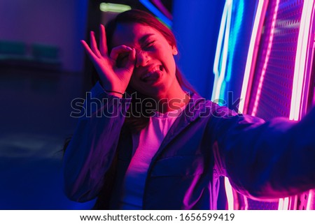 Beautiful young asian woman with long dark hair standing infront of a neon wall
