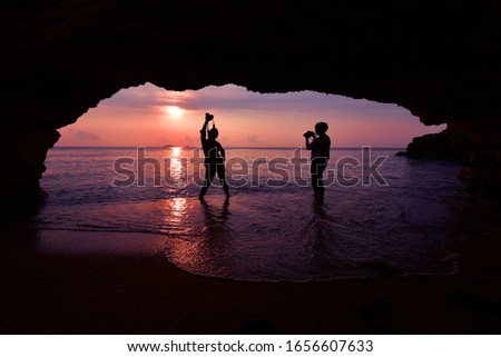 Silhouette of woman standing using camera to take a picture in front of the cave in the morning at sunrise