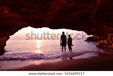 Silhouette of couple standing using camera to take a picture in front of the cave in the morning at sunrise