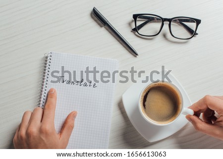 cropped view of translator with notepad, pen, eyeglasses and cup of coffee