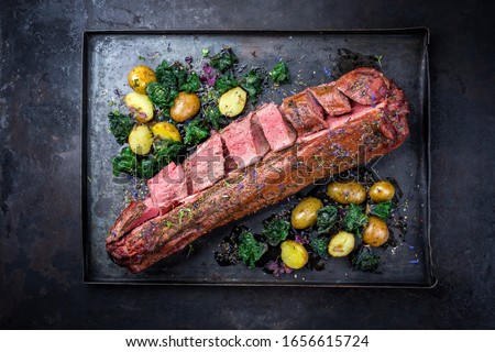 Barbecue dry aged venison tenderloin fillet steak and saddle natural with kalette and fried potatoes offered as top view on a rustic board Royalty-Free Stock Photo #1656615724
