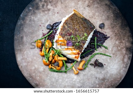 Gourmet fried European skrei cod fish filet with glasswort, fungi and algae as closeup on a modern design plate