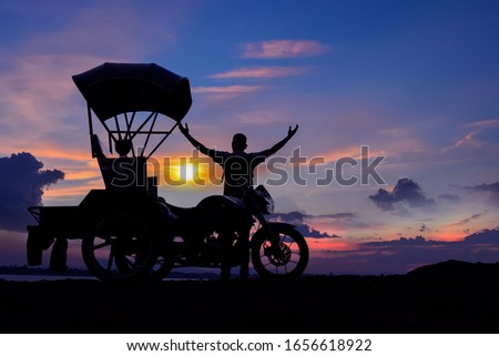 A man with a motorcycle with a roof standing watching the sunset by the river
