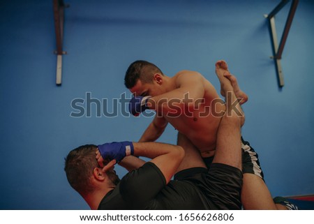 Strong MMA fighter holding his rival down and throwing punches at him during a training. With plenty of copy space