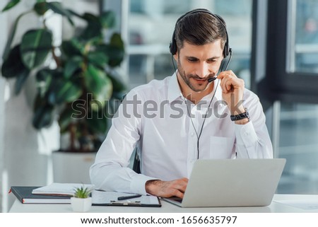 smiling male translator working online with headset and laptop