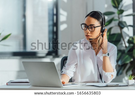 asian translator working online with headset and laptop in office