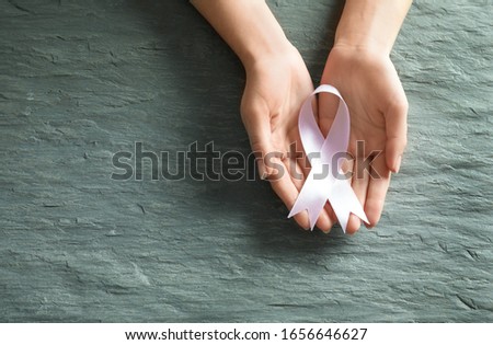 Woman holding pink ribbon on grey stone background, top view with space for text. Breast cancer awareness