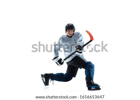 Serious. Young male hockey player with the stick on ice court and white background. Sportsman wearing equipment and helmet practicing. Concept of sport, healthy lifestyle, motion, movement, action.
