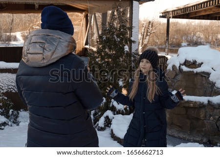 Mom takes pictures of her daughter in the park on a smartphone. Mom takes her daughter to the phone. Winter concept. Snow. Girl 9 years old blogger. Girl makes video for her pages on the Internet