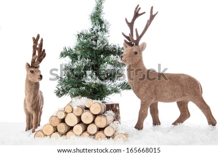 A Winter Christmas Scene with two reindeers, a couple of trunks with a Pine Tree and a Ground of snow.