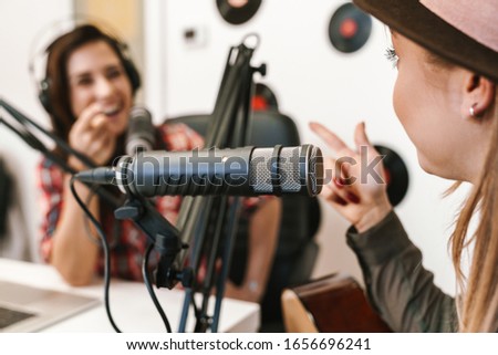 Close up of a happy woman singer performing at radio program while making podcast recording for online show, playing guitar