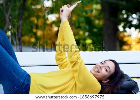 Happy girl holds in hands the smartphone taking self-portrait. Young woman has joyful expression during conversation online with her friends on social media, in the park making selfie.