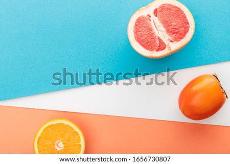 Top view of grapefruit half, slice of citrus fruit and persimmon on blue, orange and white background