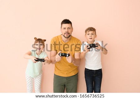 Father and his little children playing video games on color background