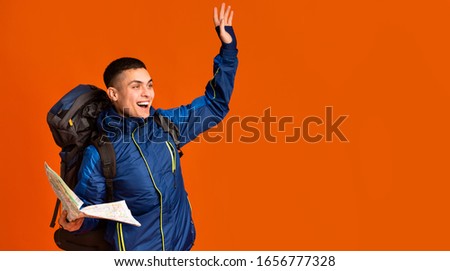 Emotional backpacker with map found a place, gesturing over orange background, looking at copy space