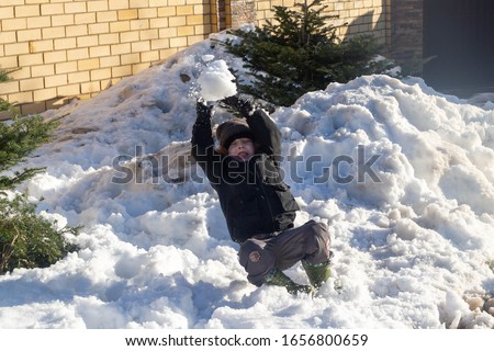 An active cheerful boy makes a lump of snow. Warm weather in winter.