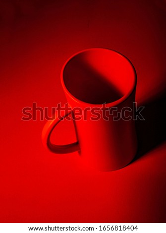 One red ceramic mug on red background.