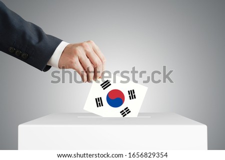 Man putting a voting ballot into a box with South Korea flag.