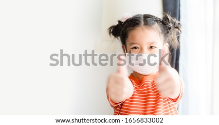 Coronavirus Covid-19 pm2.5.Online education.Little chinese girl wearing face mask show thumbs up for good and happy at home. Covid-19 coronavirus.Stay home.Social distancing.New normal behavior. Royalty-Free Stock Photo #1656833002