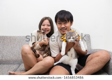 Asian girls and boys playing with cats on the sofa in the house.Asian lovers taking pictures with cats inside the home.
