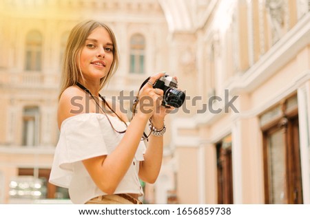 Portrait of young attractive tourist woman with a retro camera in her hands while posing at urban old architecture. Discover new places