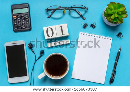 Office workplace with coffee cup, smart phone, calculator, stationery and plant. Date 01 March on wooden block calendar. White blank empty notepad page. Table desk top view, flat lay, copy space