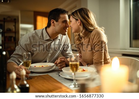 Romantic couple about to kiss while holding hands during dinner at dinning table.  Royalty-Free Stock Photo #1656877330