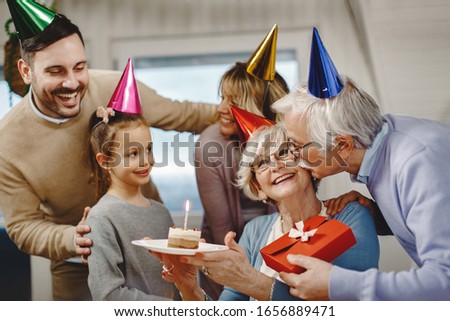 Senior man kissing his wife while celebrating her Birthday with their family at home. 
