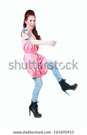 Pretty young woman wearing pink dotted dress, ripped jeans, black boots with high heels and spikes, moving, dancing, smiling at camera. Isolated on white