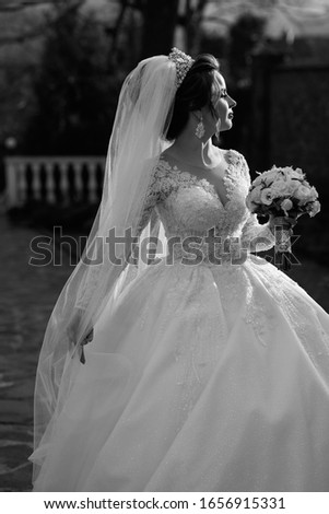 Bride holds a wedding bouquet of white flowers. Bride posing outdoor. Portrait with natural light of young beautiful woman with stylish make-up and hairstyle. Black and white photo