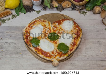 Home made heart shaped pizza served on wooden board, with vegetables decoration.