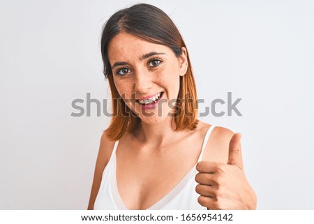 Beautiful redhead woman wearing casual white t-shirt over isolated background happy with big smile doing ok sign, thumb up with fingers, excellent sign