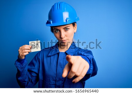 Beautiful worker woman wearing hardhat and uniform celebrating 8th march womens day pointing with finger to the camera and to you, hand sign, positive and confident gesture from the front