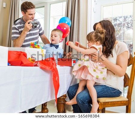 Family opening birthday presents with man taking picture through camera