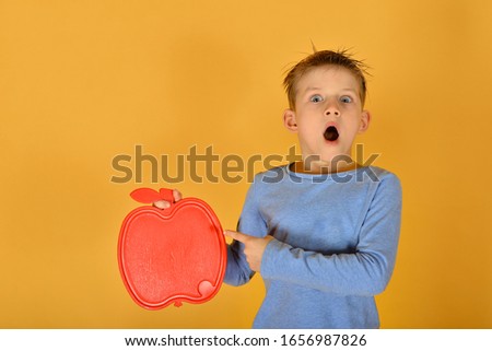 The boy holds in his hand a blank red plate in the form of an apple, a place for advertising or inscription.