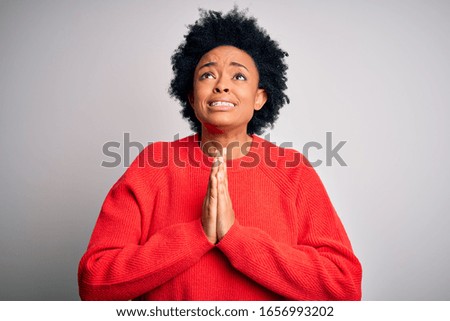 Young beautiful African American afro woman with curly hair wearing red casual sweater begging and praying with hands together with hope expression on face very emotional and worried. Begging.