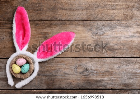 Headband with bunny ears, painted eggs and space for text on wooden background, flat lay. Easter holiday