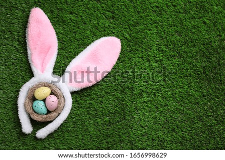 Headband with bunny ears, painted eggs and space for text on grass, flat lay. Easter holiday