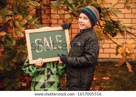 Two boys point to the inscription on the plate. Advertising in the hands of children. The boys are happy and smiling, laughing. Autumn sales, discounts, cheap prices. Autumn came, yellow leaves.