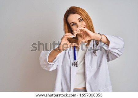 Redhead caucasian doctor woman wearing stethoscope over isolated background smiling in love showing heart symbol and shape with hands. Romantic concept.